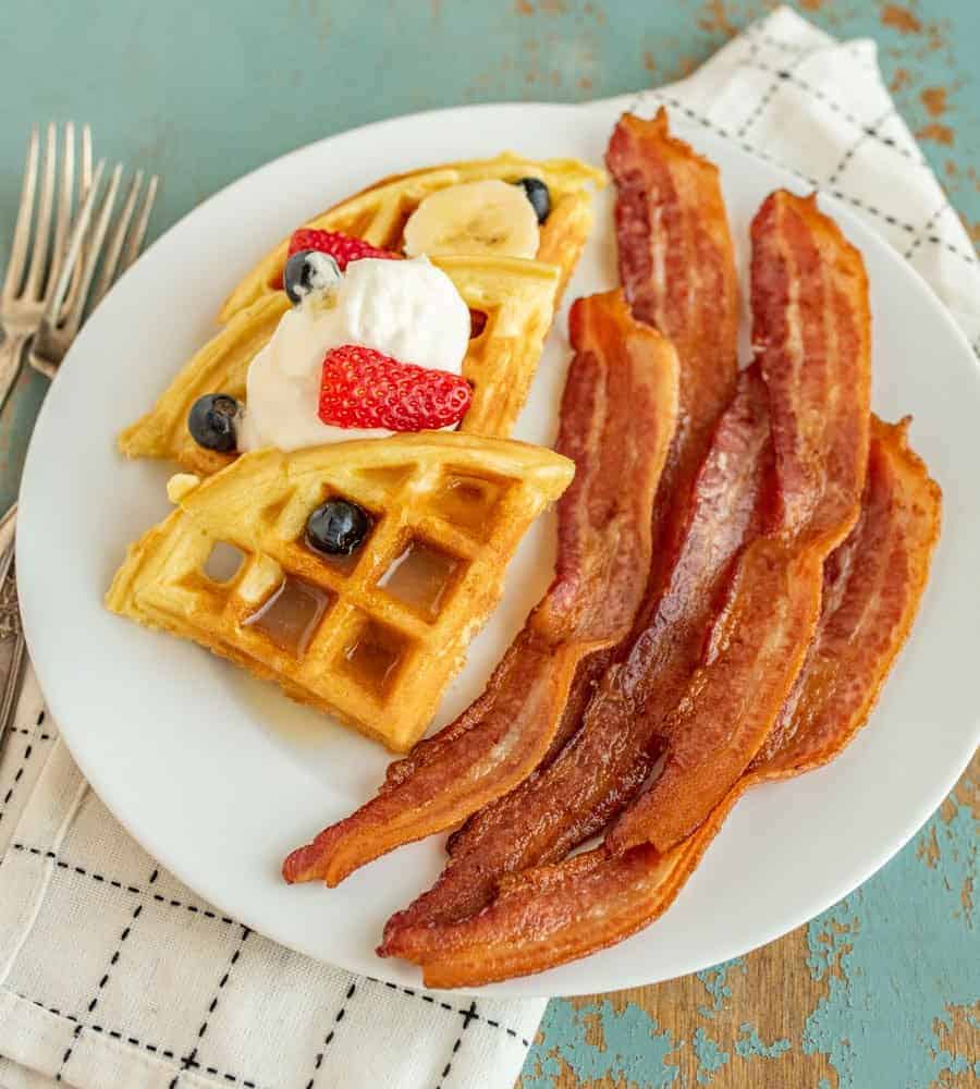 Tips and tricks you need to know so that you can cook crispy bacon in a cast iron skillet any day of the week. Bacon and waffles on a plate.