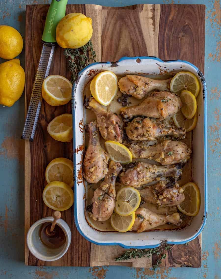 An overhead shot of baked lemon garlic chicken legs in a pan resting on a cutting board.