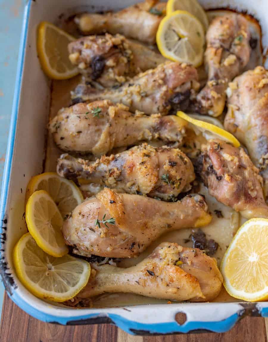 A close up of lemon garlic baked chicken legs sitting in a baking dish topped with lemon slices.