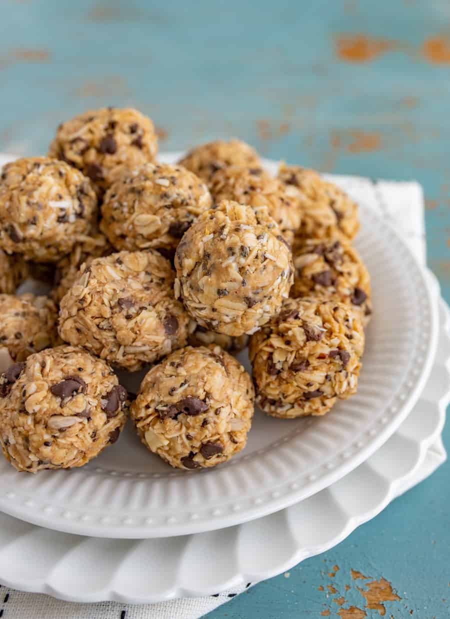 A white plate is filled with oatmeal protein balls made from oats, chocolate chips, and seeds, set on a textured blue surface. The bites are round and appear homemade.