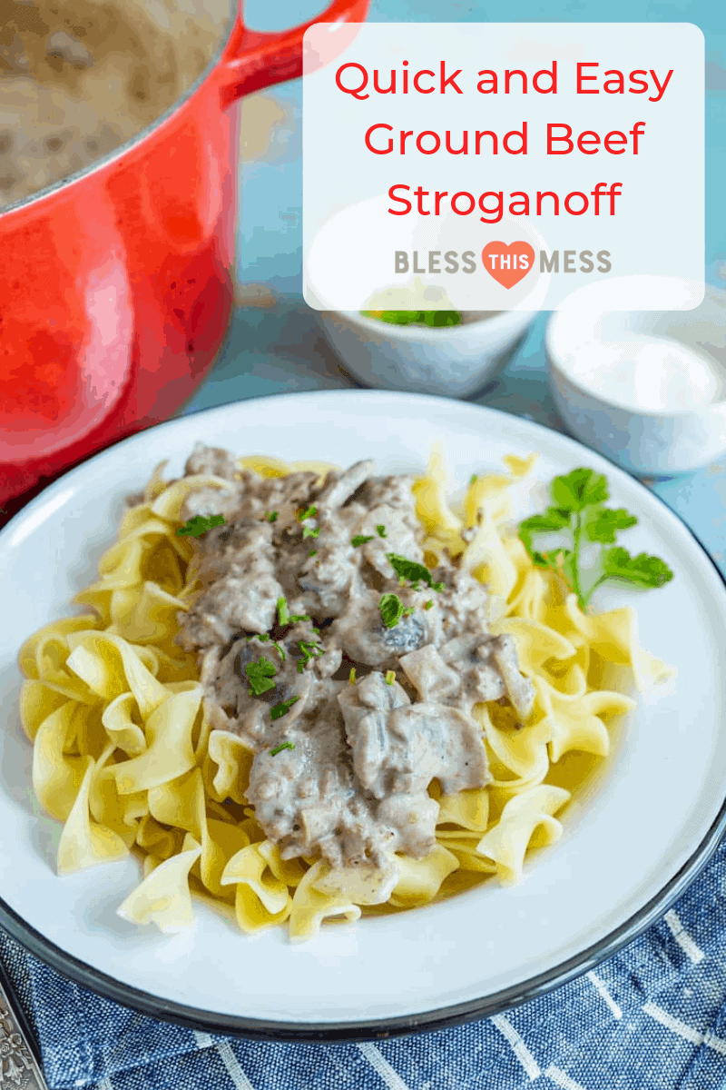 egg noddles on a white plate with ground beef and white sauce on top with green parsley and forks next to it with white bowls and red pan in background.