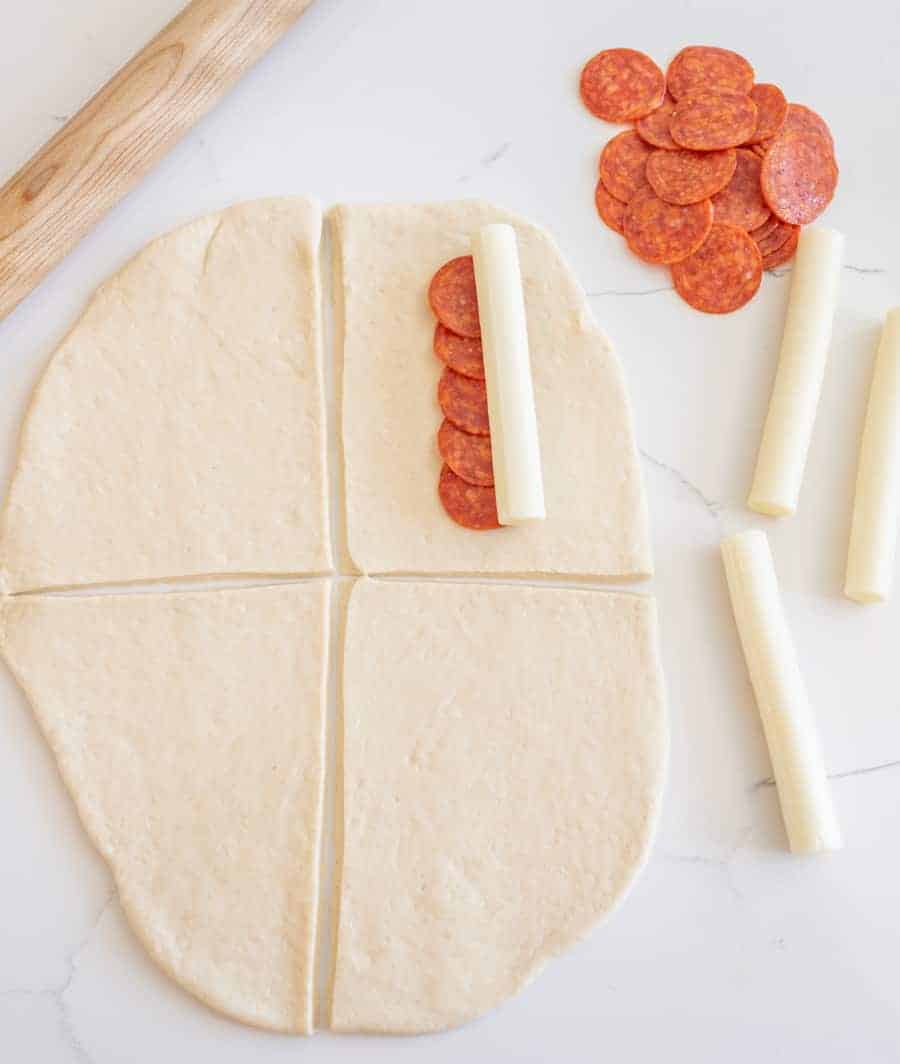 rolled out dough on white marble background with white cheese sticks and pepperoni slices.