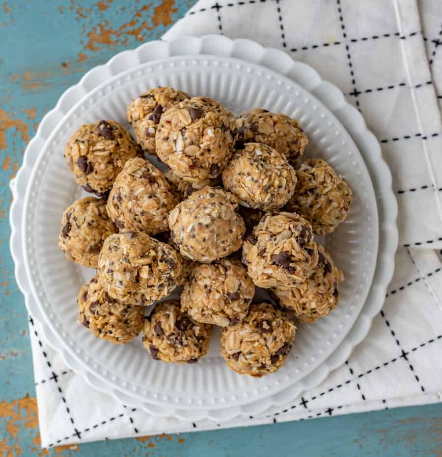 balls of oats, peanut butter, chocolate chips, and other ingredients on a white plate set on a white and white towel.