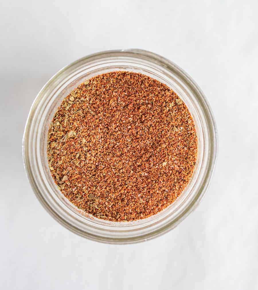 round clear glass jar with spice mix of multiple colors on a white background.