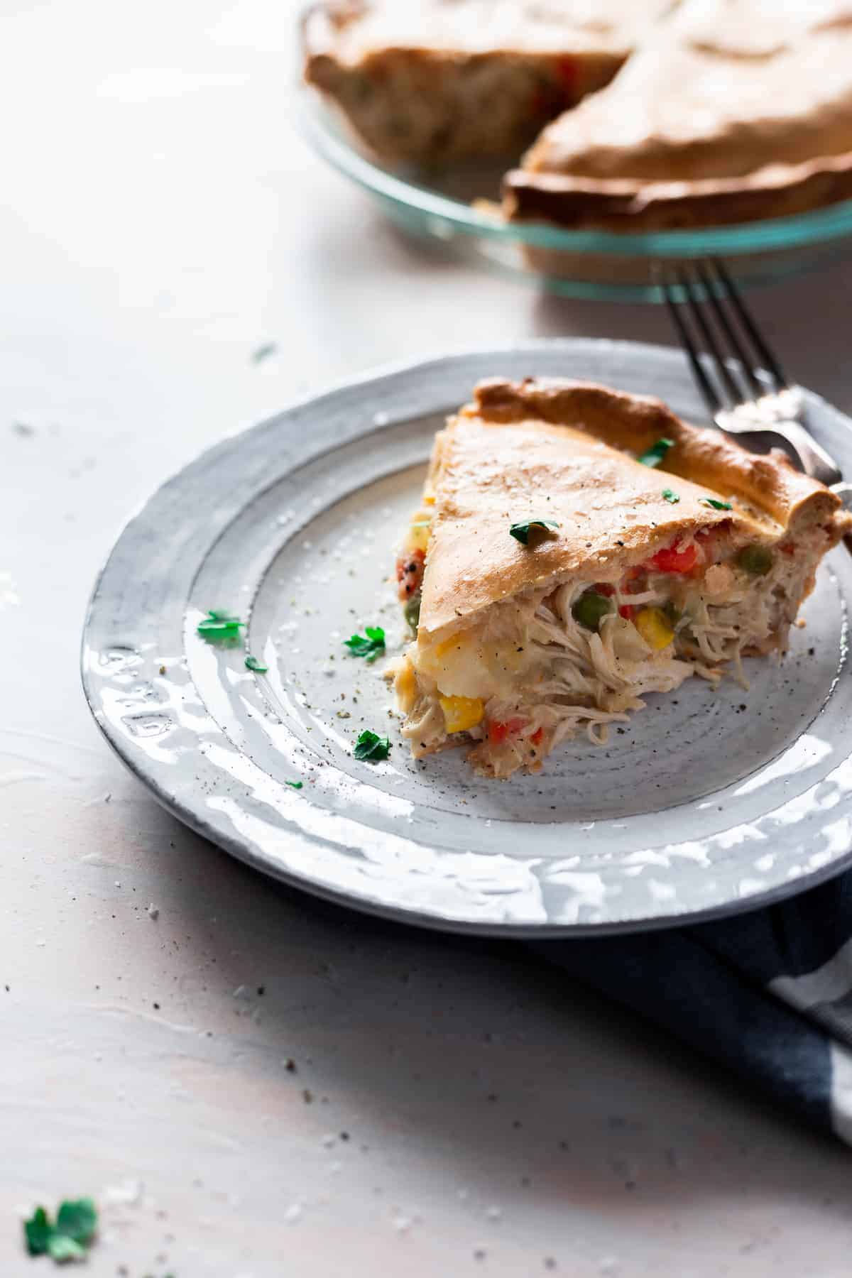 slice of baked pie crust filled with chicken, corn, peas, and carrot mixture on a plate with fork.