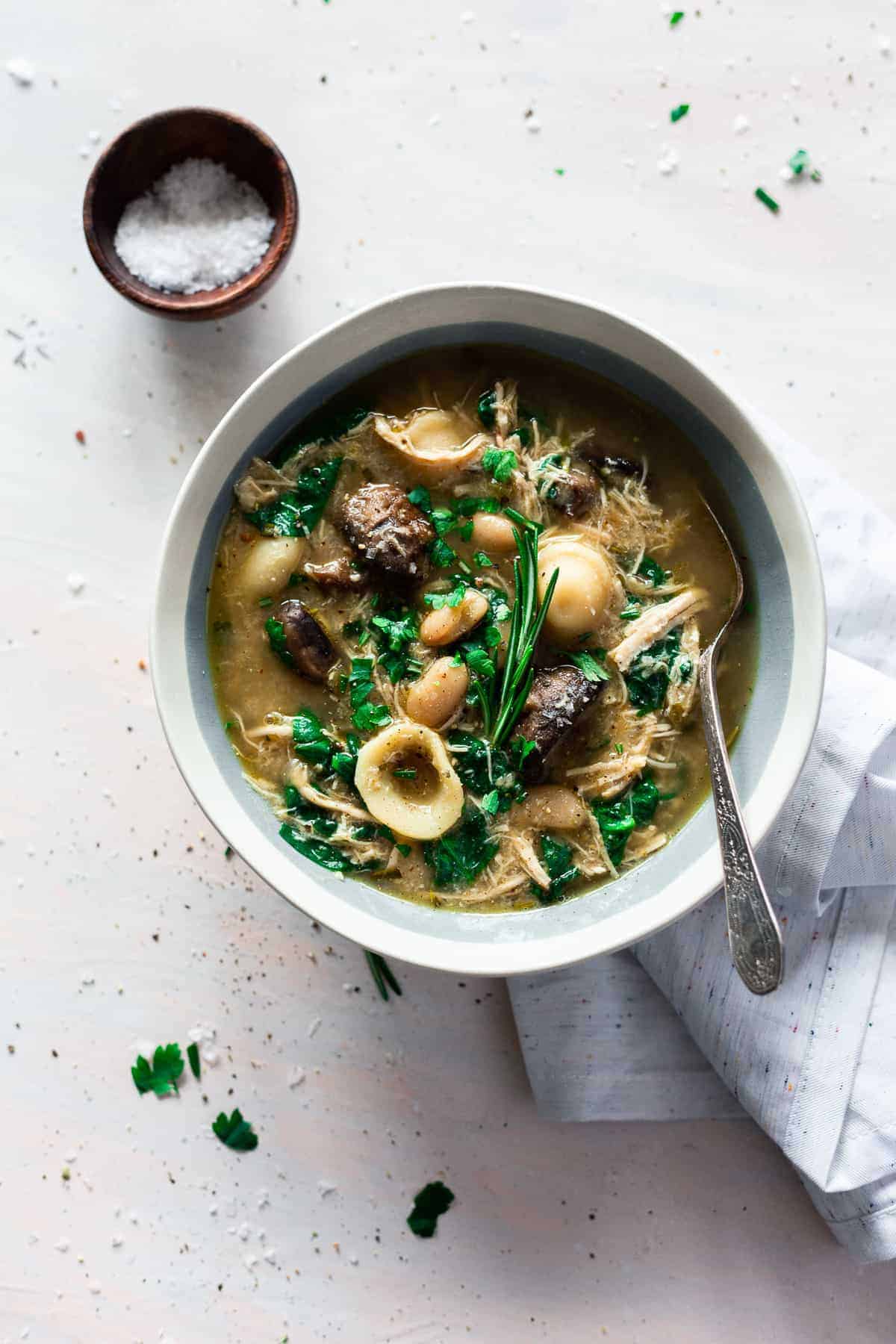 Italian chicken and mushroom soup in a white and blue bowl salt in a bowl in background.