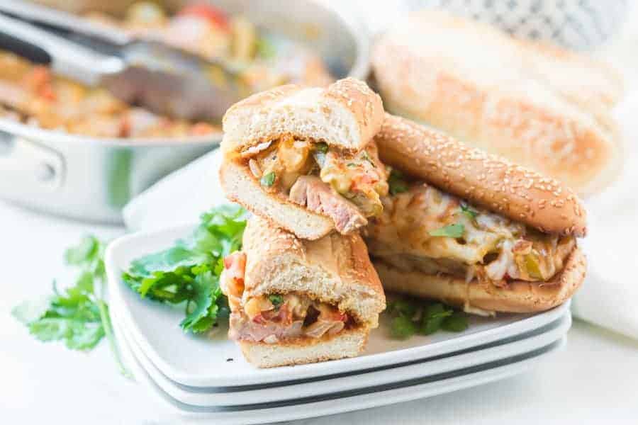 Cheese steak sandwich sesame bun stuffed with melty classic cheesesteak ingredients with parsley on a stack of three white plates.