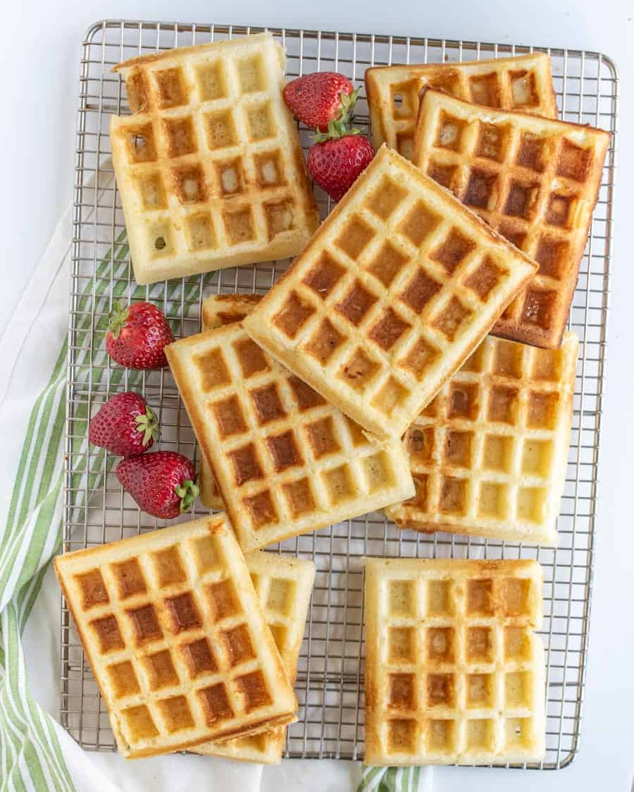 waffles on a plate with syrup and strawberries on a cooling rack.