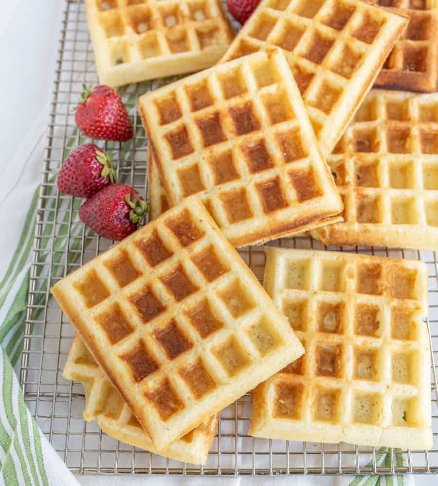 buttermilk waffles on a plate with syrup and strawberries on a cooling rack.