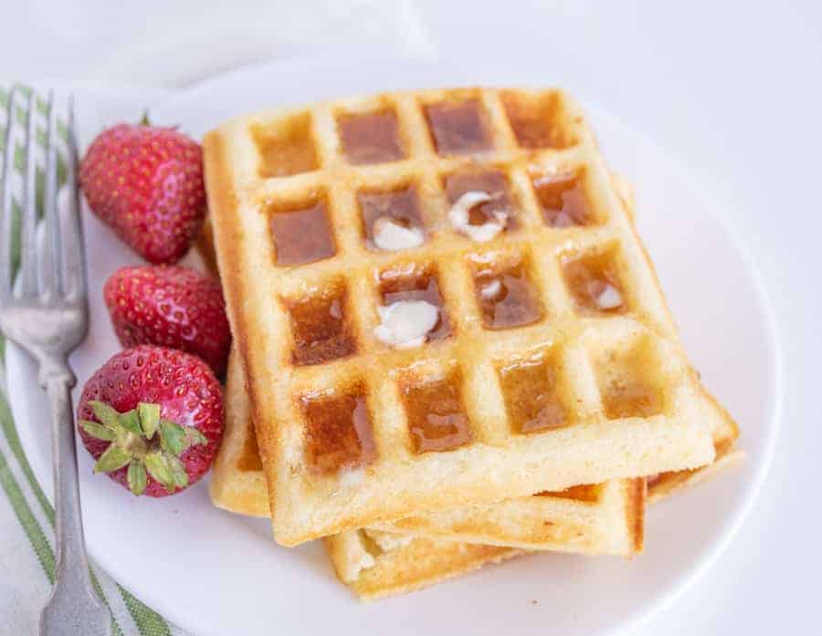 waffles on a plate with syrup and strawberries.