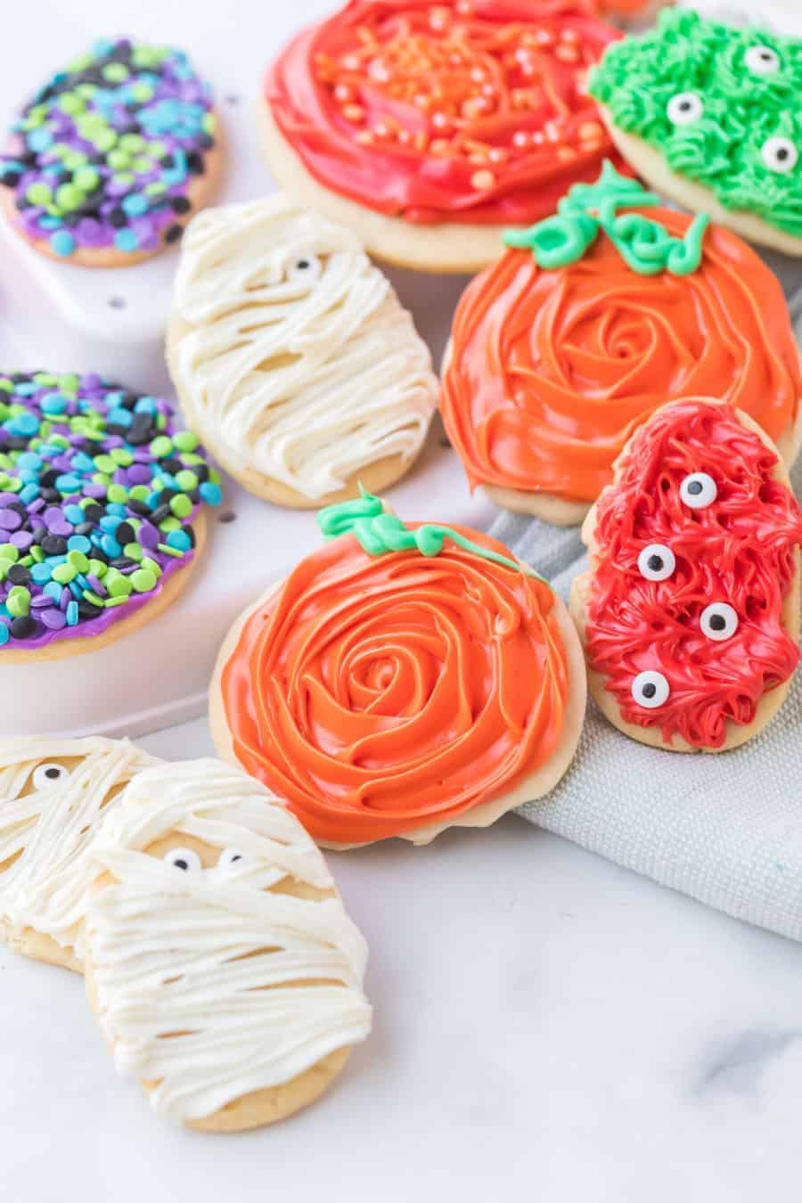 sugar cookies decorated with halloween theme white frosting to look like a mummy with candy eyes and colored sprinkles in purple black green and blue colors and orange and green icing to look like pumpkins red and green icing with eyes to look like monsters.