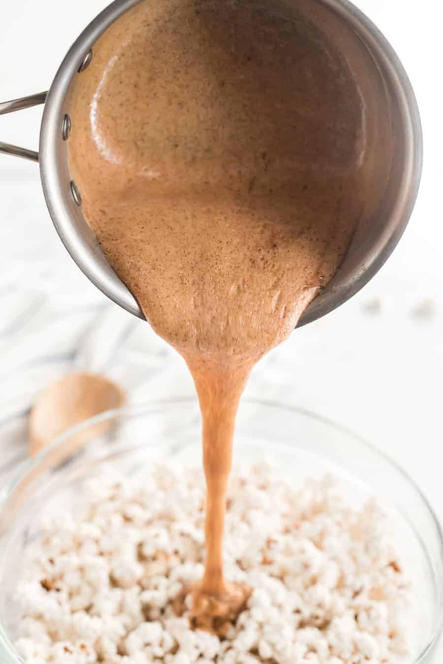 honey caramel being poured over a glass bowl of popcorn.