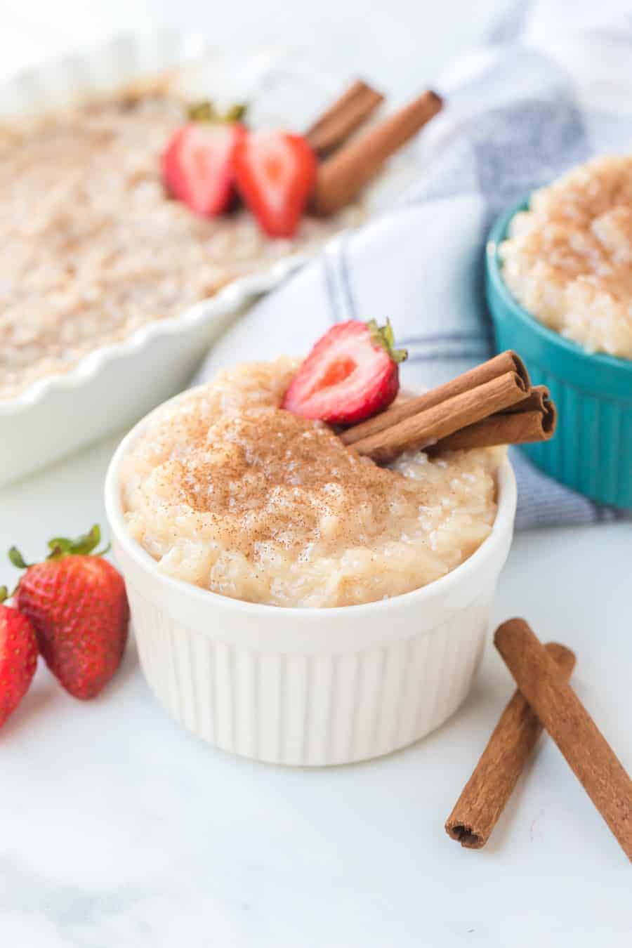 Rice pudding in white ramekin with strawberries and cinnamon sticks.