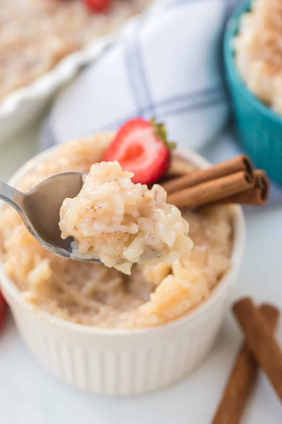 Rice pudding in white ramekin with strawberries and cinnamon sticks.