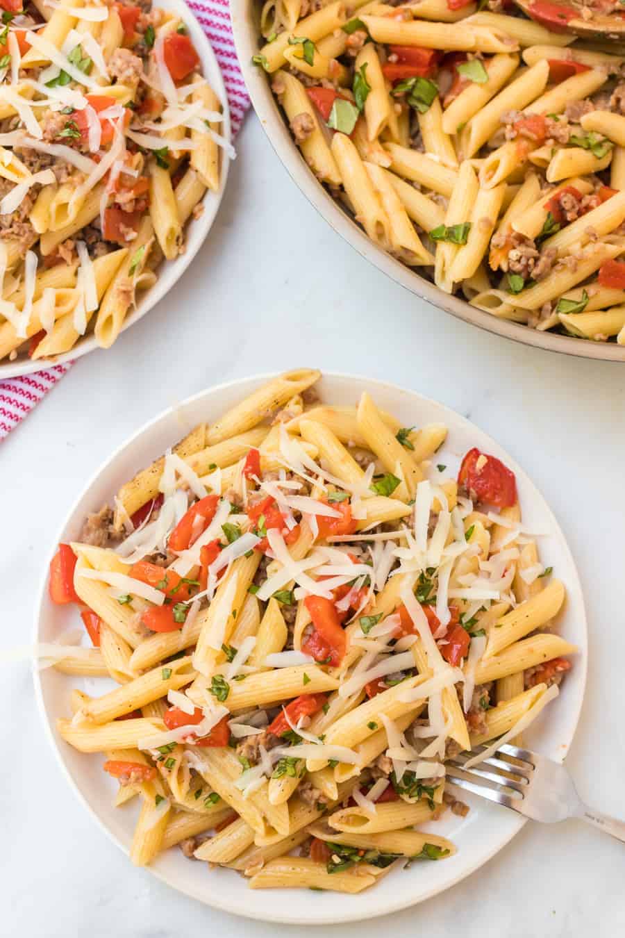 pene pasta with shredded cheese with tomatoes and herbs on a white plate.