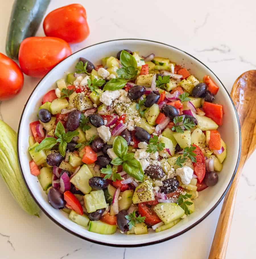 cucumber and tomato salad with olives and basil in a white bowl
