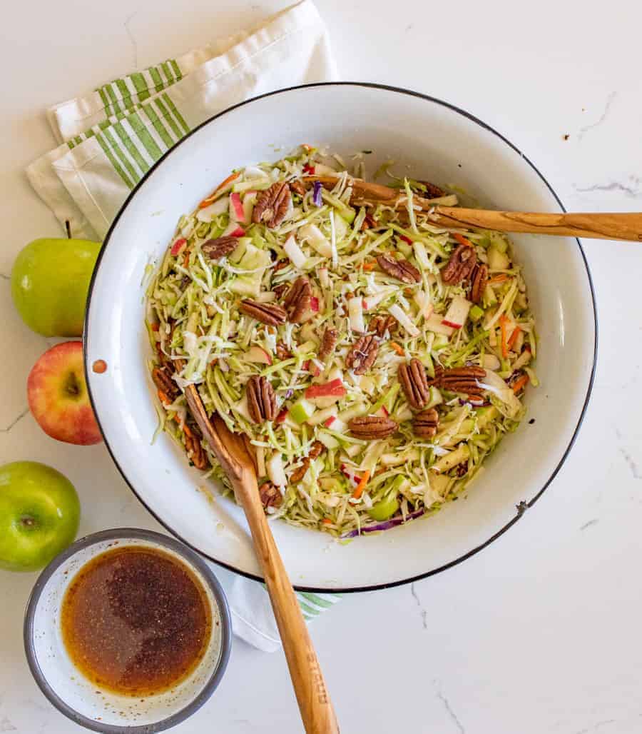 upclose image of apple cabbage salad topped with pecans with a dressing being spooned on top.
