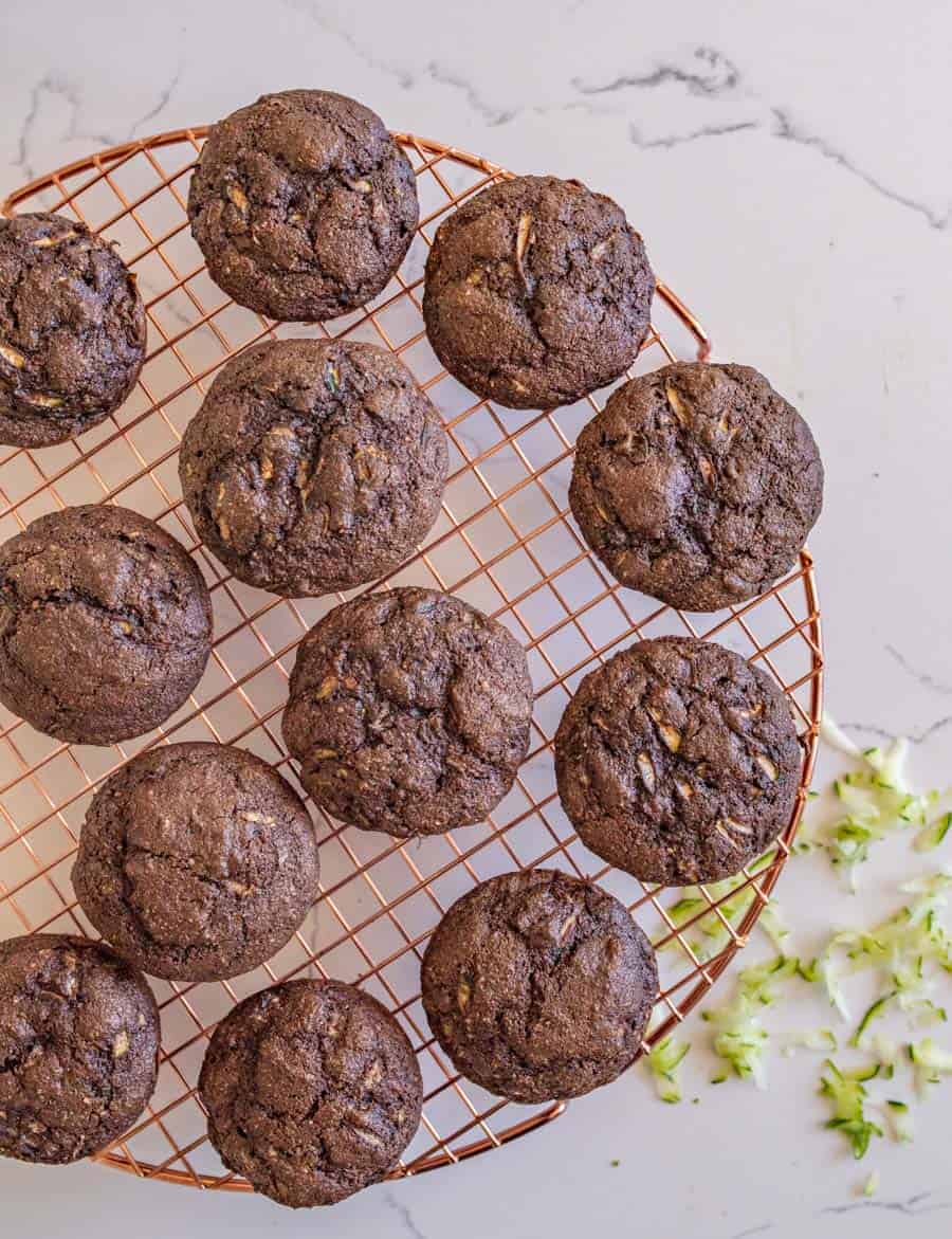 chocolate muffins on a copper colored round wire rack on a white marble table.