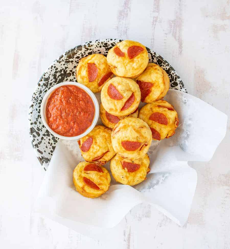 Pizza muffins sitting on a plate with marinara sauce in a bowl on the side.