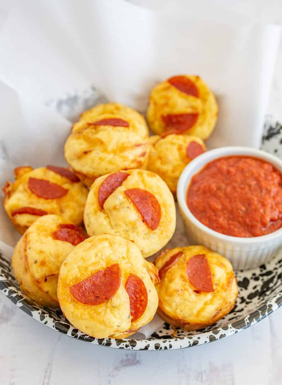 pizza bites with marinara dipping on parchment in a bowl.