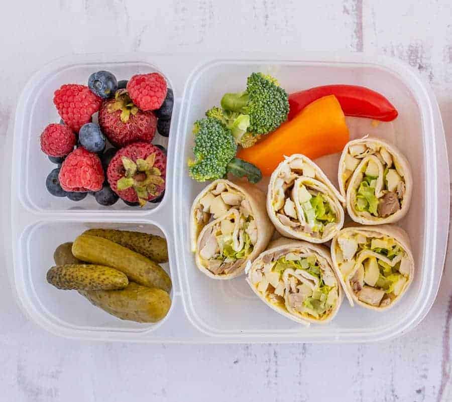 A lunchbox with sections containing chicken wrap pinwheels, sliced pickles, fresh raspberries and blueberries, strawberries, broccoli florets, and red and orange bell pepper strips—perfect inspiration for easy pinwheel recipes.