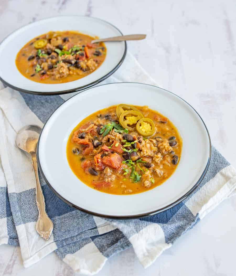 sausage black bean and pumpkin soup showing soup in white bowls with gold spoon on a blue and white dish towel.