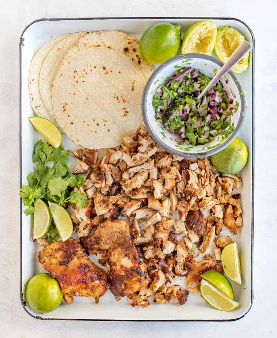 lime wedges, cilantro, red onion, chicken and tortillas on white tray.
