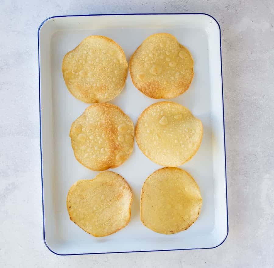 toasted tostada rounds on white pan with blue rim on a white countertop.