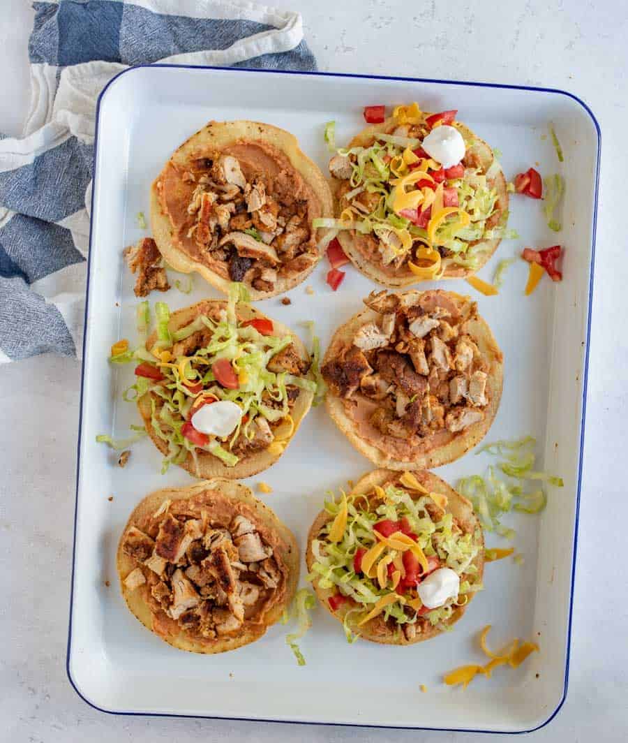 grilled chicken on tortilla rounds on a white pan with lettuce cheese and tomatoes.