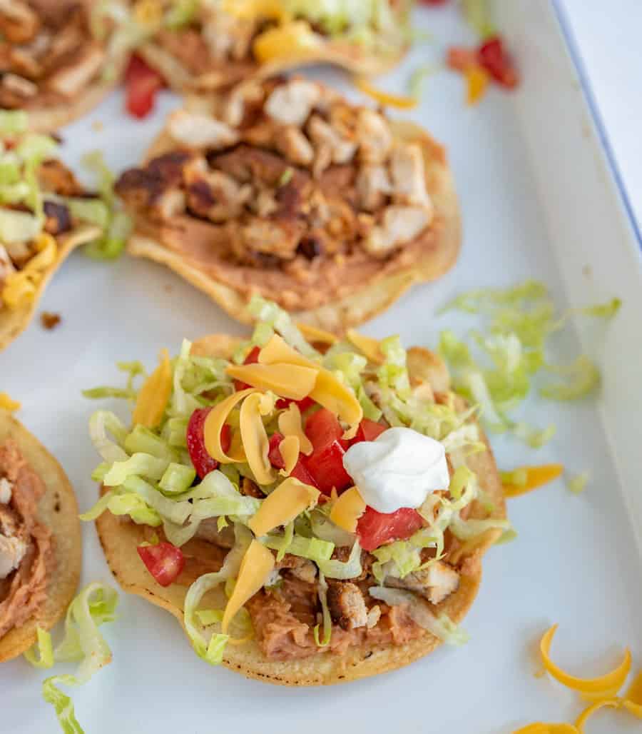 grilled chicken on baked tortilla shell on a white pan with lettuce cheese and tomatoes.