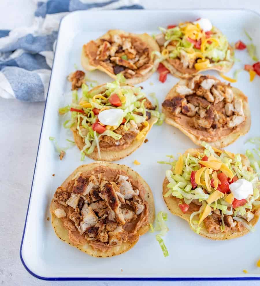 Chicken tostadas on a white pan with lettuce cheese and tomatoes.