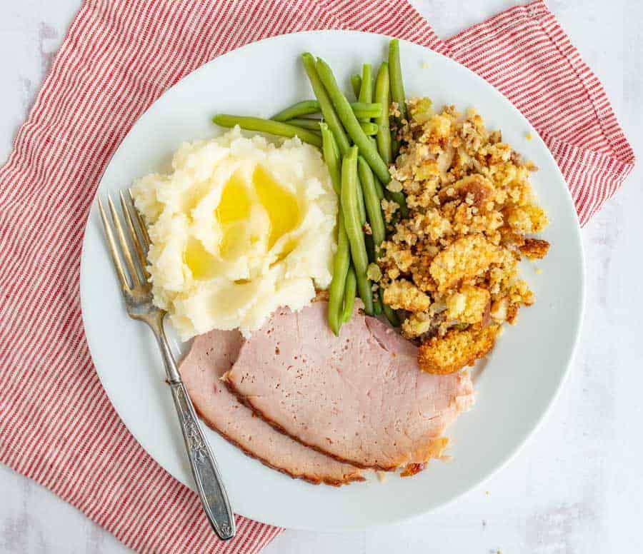 ham mashed potatoes green beans and stuffing on a white plate.