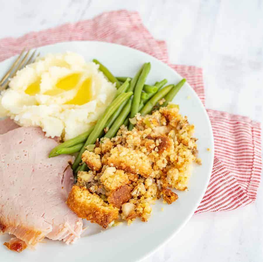 ham mashed potatoes green beans and stuffing on a white plate.