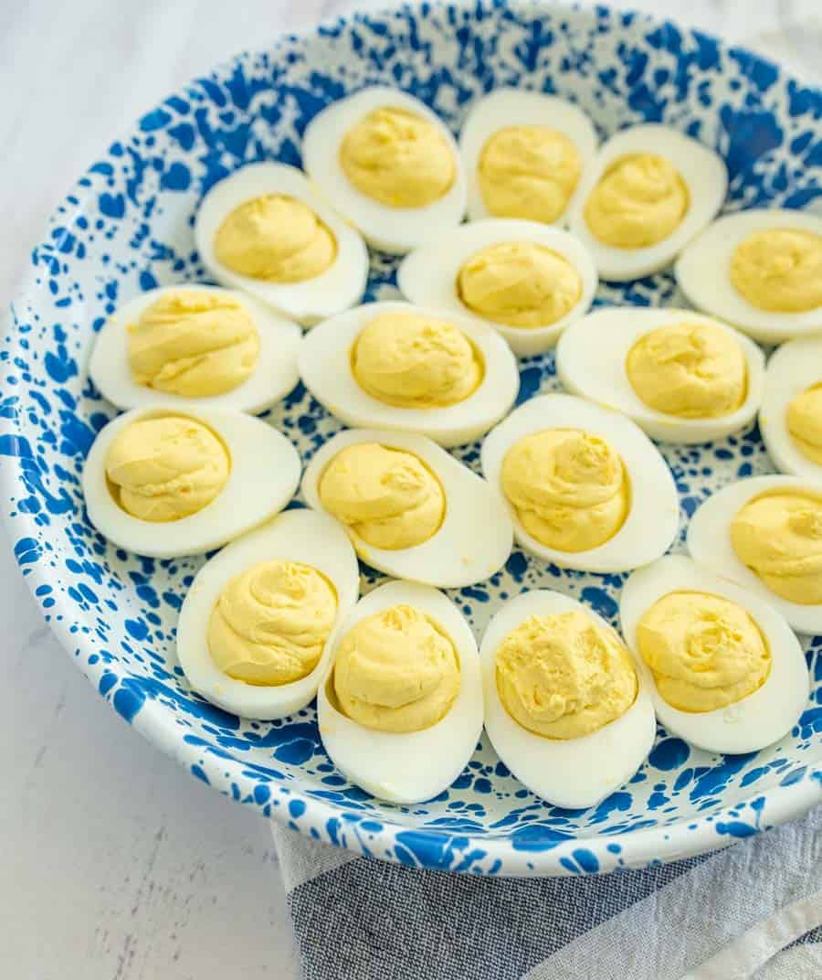 closeup deviled eggs in blue and white bowl on white countertop.