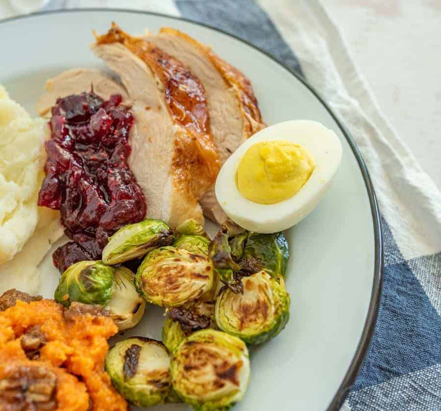 round white plate with black trim with brussels sprouts deviled eggs roast turkey sweet potato casserole cranberry sauce.