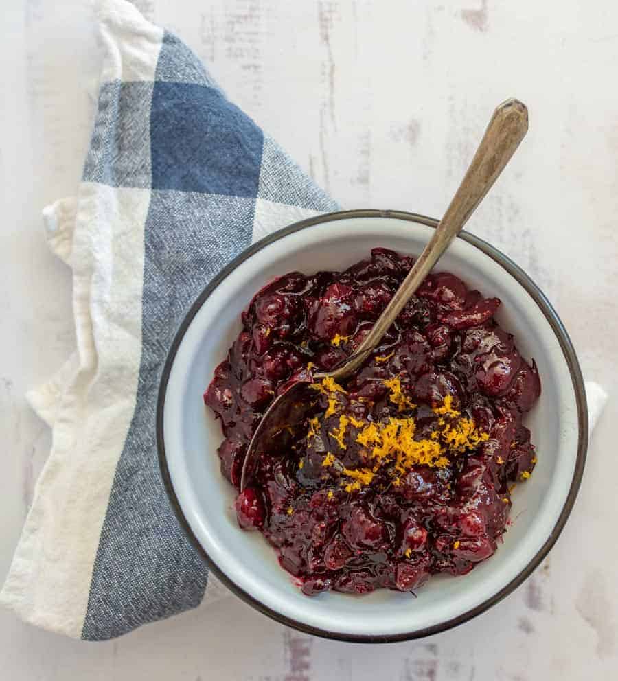 white bowl with homemade cranberry sauce and orange zest on tip with spoon.