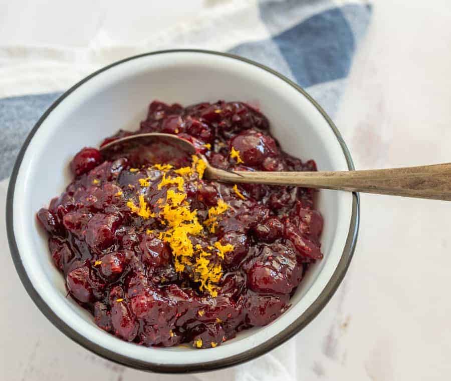 white bowl and spoon with red cranberry sauce and orange zest.