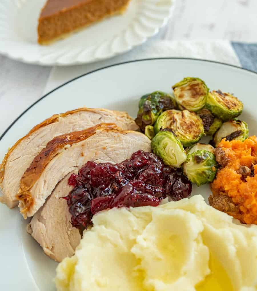 white place with turkey potatoes cranberry sauce brussel sprouts and sweet potatoes.