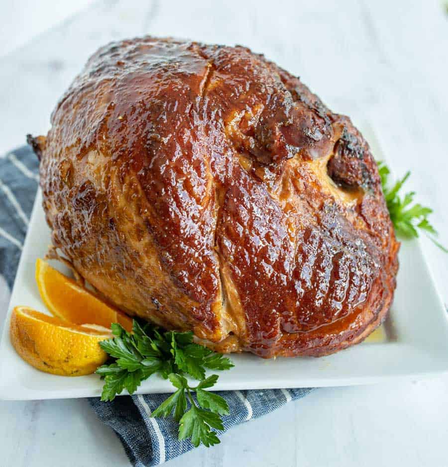 whole cooked brown sugar glazed ham on white plate.