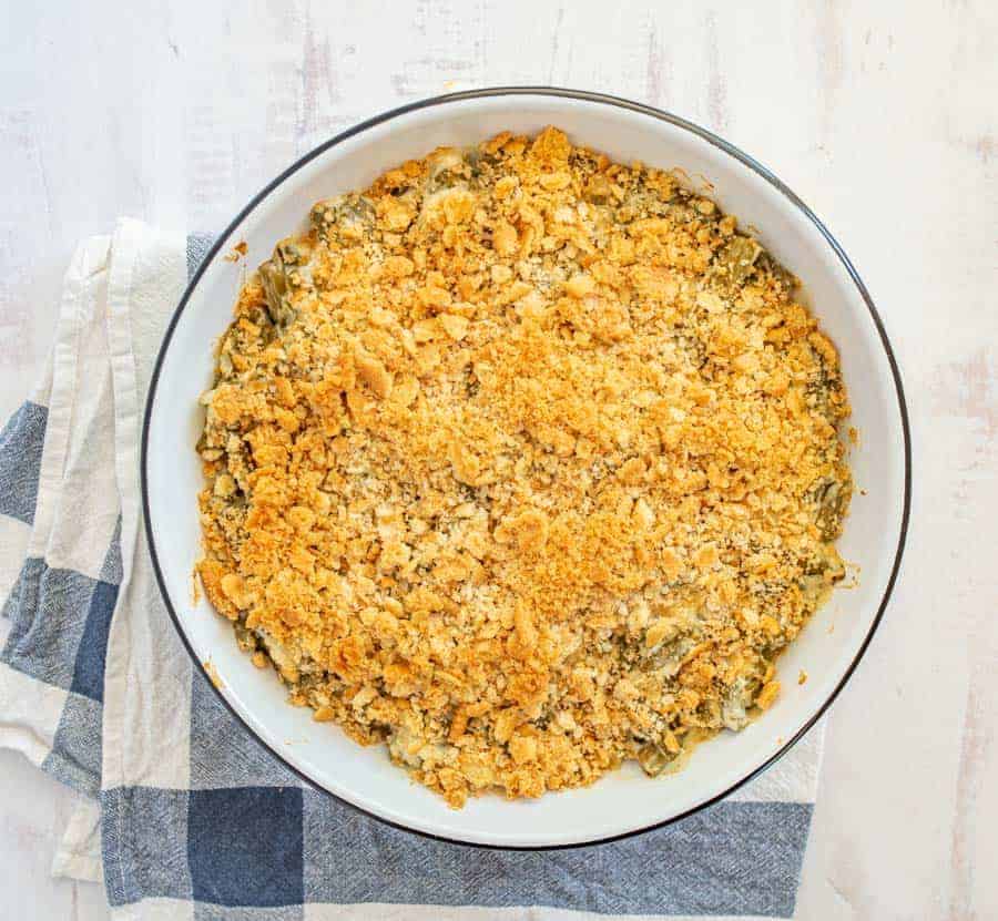 Green bean topped with cracker crumbs in white baking dish on blue and white towel.