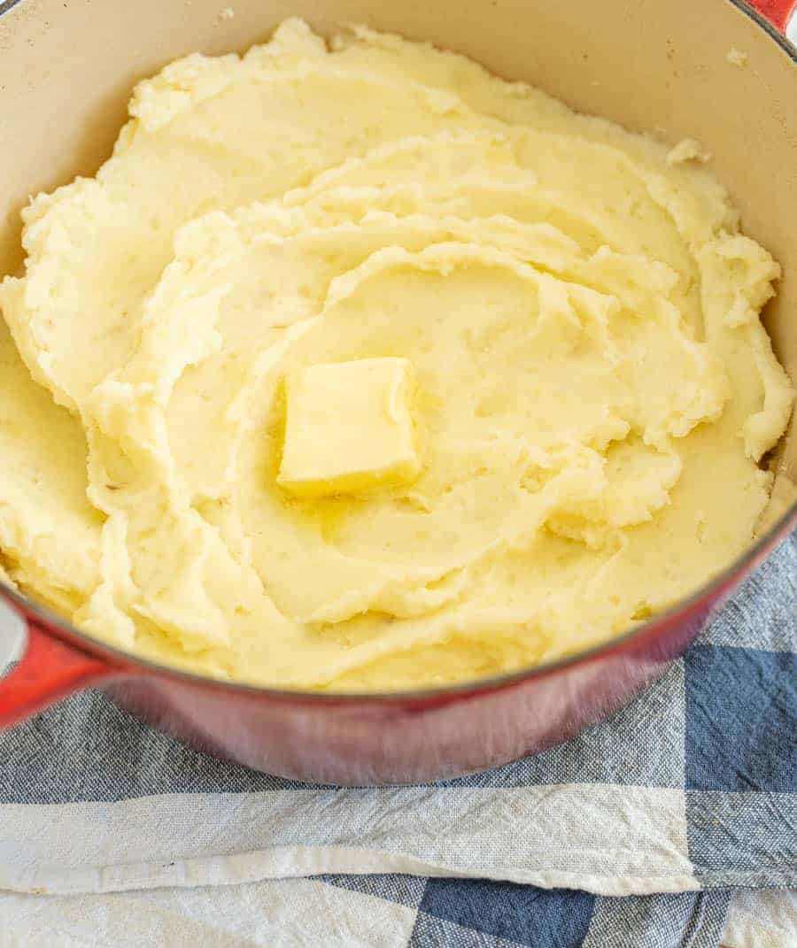 mashed potatoes in red dutch oven with butter melting.