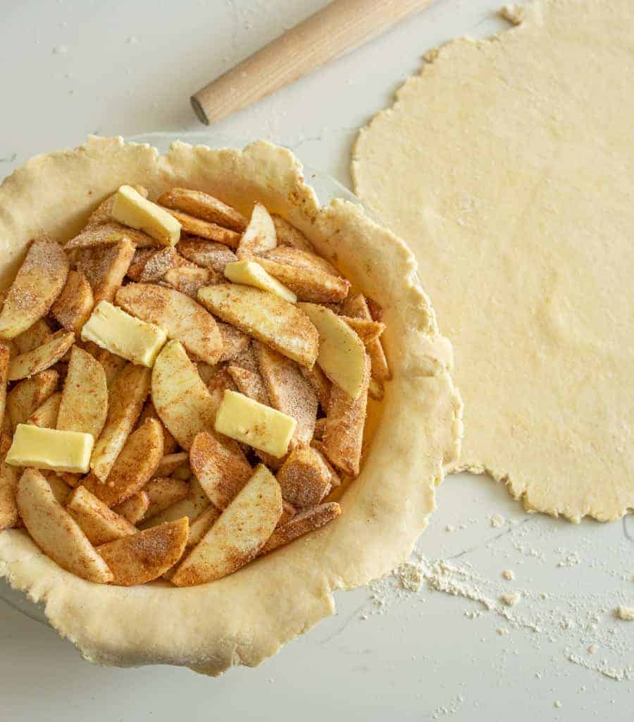 butter and seasoned apple slices inside a rolled out pie crust inside the pie dish all raw.