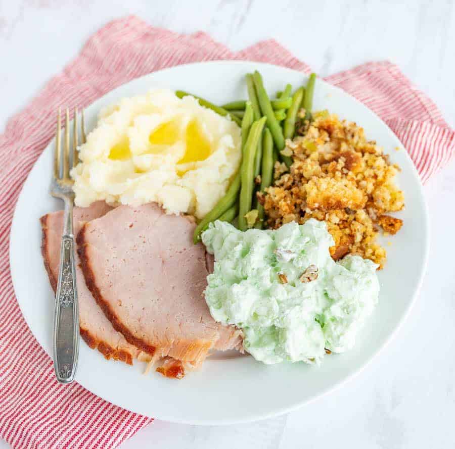 Thanksgiving dinner on a plate, ham, mashed potatoes, green beans, stuffing, and pistachio salad.