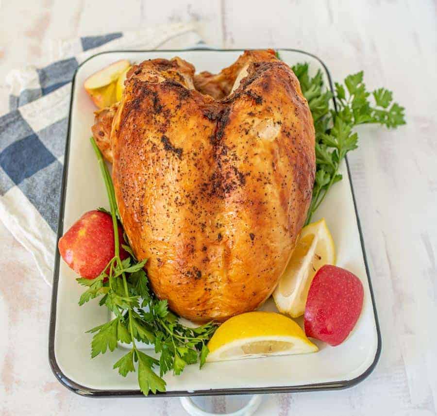 A roasted turkey with apples, lemon, parsley, and thyme in a white ceramic pan.