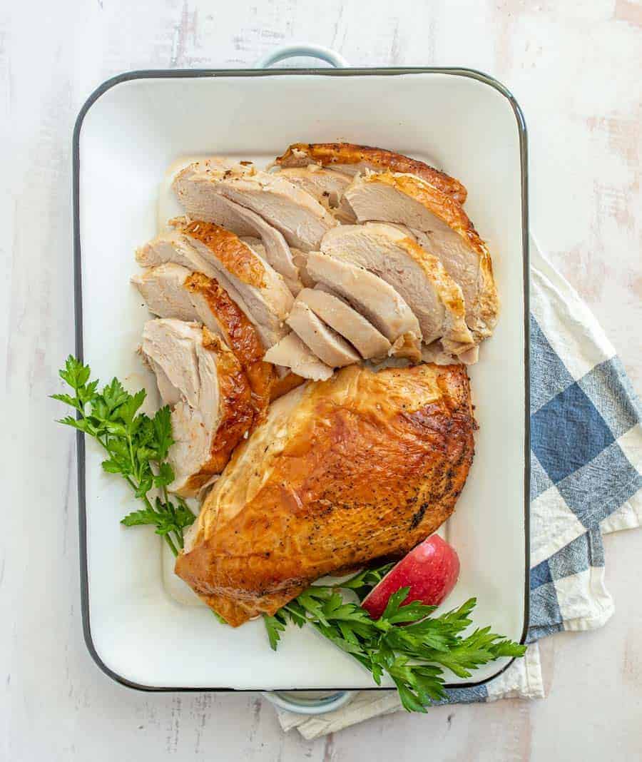 Sliced roasted turkey with parsley, thyme, and apple in a white pan.