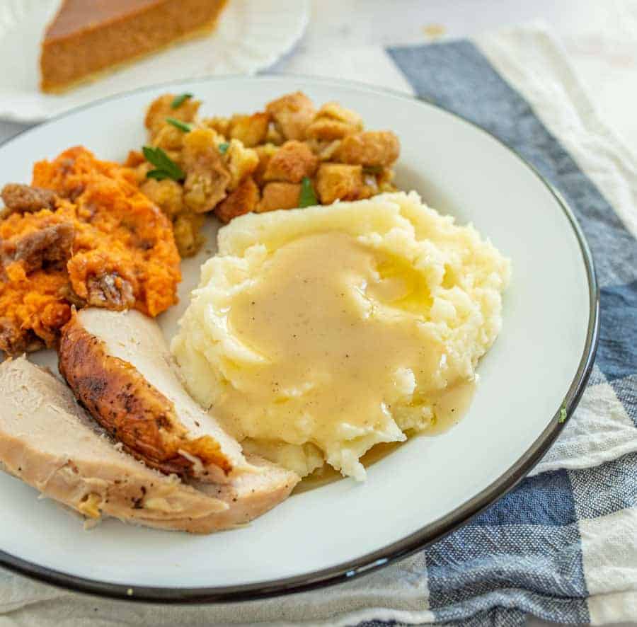 White plate with mashed potatoes and gravy and turkey breast with other sides.