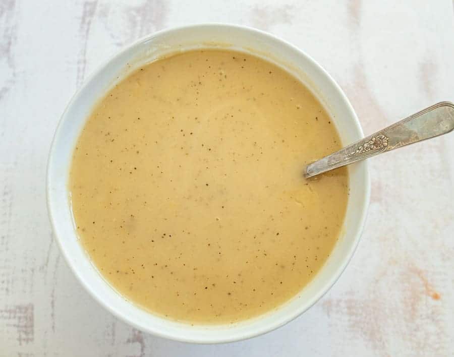 white bowl with creamy light brown turkey gravy and a silver spoon.