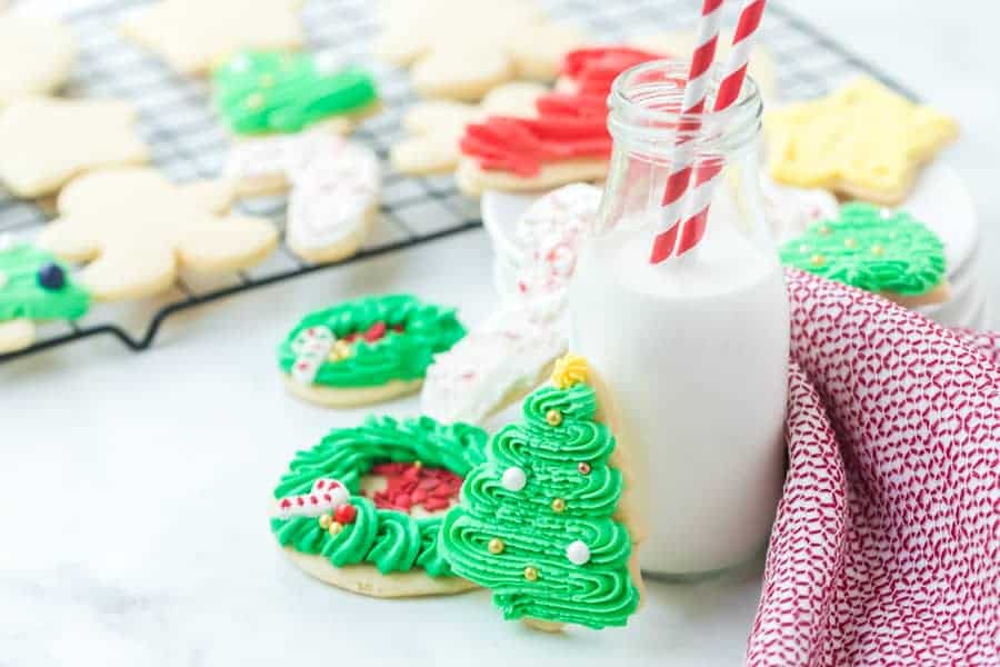 holiday decorated sugar cookies iced next to a glass jug of milk.