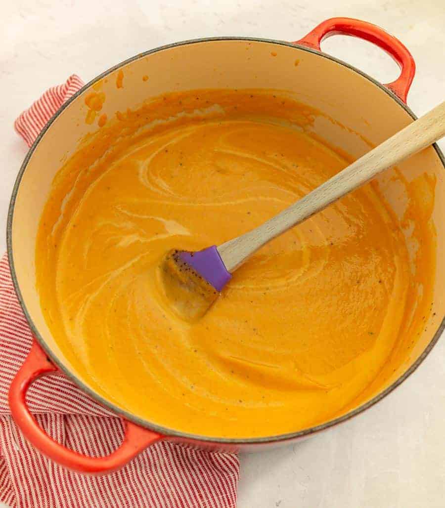 red dutch oven with soup and stirring spoon inside.