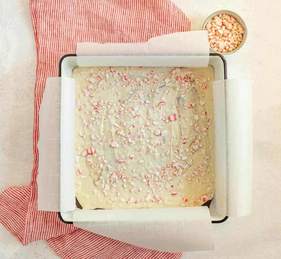 A shot of peppermint bark in a white square pan with a green outline, resting on top of a red and white striped towel.